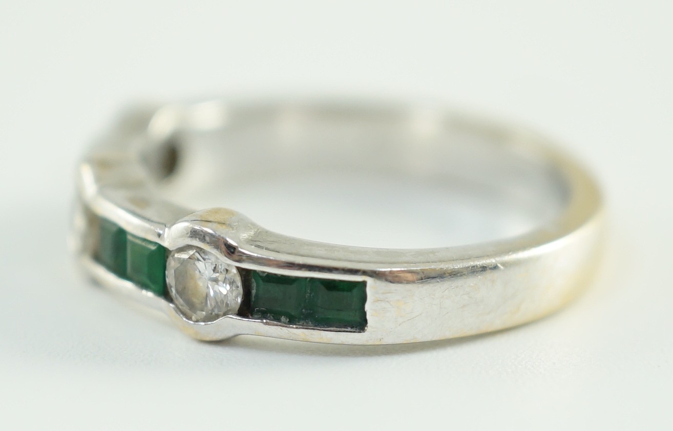 A modern 18ct white gold, three stone collet set diamond and eight stone channel set emerald half hoop ring